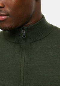 Dark green knit sweater with a high collar and half zipper. Features ribbed texture and subtle detailing along the zipper line.