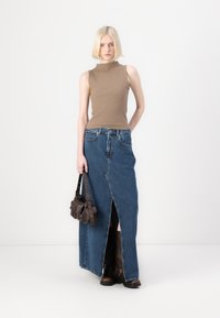 Rjava brezrokavnik v kombinaciji z visokim denim maxi krilom z bočnim razporkom, ki ga dopolnjuje temno rjava torba za rame in črne škornje.