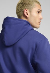 Felpa blu reale con cappuccio regolabile e cuciture visibili, realizzata in tessuto testurizzato, che mostra una vestibilità comoda dalla vista laterale.