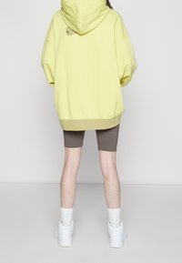 Överdimensionerad gul hoodie med huva, bruna shorts och vita sneakers. Har en liten accentdetalj på baksidan av hoodien.