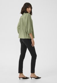 Blusa verde chiaro a maniche corte con maniche a sbuffo e dettagli in pizzo lungo le cuciture, abbinata a jeans neri aderenti e mule nere.