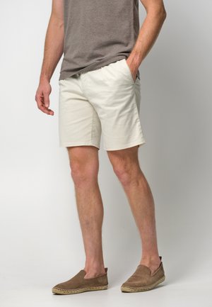Shorts beige clair en coton, avec une coupe décontractée, des poches latérales et un design à l'avant plat. Associés à des chaussures brunes à enfiler.