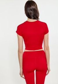 Rød atletisk crop top med korte ærmer og tætsiddende design, parret med matchende højtaljede leggings. Glat, strækbart stof uden mønstre.