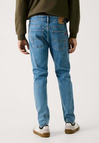 Lys blå denim jeans med slim fit, med to baklommer, subtile sømdetaljer og et brunt skinnmerke i midjen.