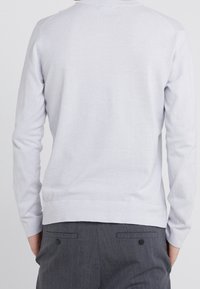 Jasnoszary sweter z długim rękawem o gładkiej fakturze, z okrągłym dekoltem, ściągaczem w dole oraz dopasowanymi rękawami, zestawiony z ciemnoszarymi, dopasowanymi spodniami.