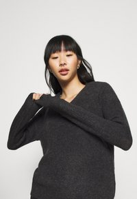 Dunkelgrauer Strickpullover mit V-Ausschnitt, langen Ärmeln und weicher Textur. Hat eine lockere Passform und gerippte Manschetten. Minimalistisches Design.
