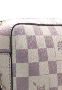 Fioletowa i kremowa torba w kratkę ze skóry, z zamkiem błyskawicznym, teksturowaną powierzchnią i kwiatowymi akcentami. Krawędzie są obszyte w dopasowanym kolorze.