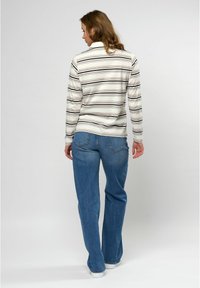 Gestreepte lange mouw top in beige en marineblauw, met een kraag, gecombineerd met uitlopende blauwe jeans en witte sneakers. Vlakke achterkant zichtbaar.