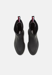 Botas de tobillo impermeables negras con un exterior de cuero suave, suela de goma acanalada y una lengüeta de tirón a rayas en rojo, blanco y azul.