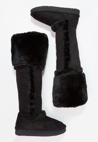 Svarta knähöga stövlar i mocka med foder av konstpäls. Har en kraftig sula, mjuk textur och en bred, fluffig kant högst upp.