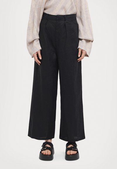 Črne široke hlače iz lahkega materiala z naborki na pasu, v kombinaciji s črnimi platformami, ki imajo pletene trakove.