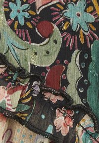 Tessuto nero con motivi floreali e astratti in turchese, rosso e rosa, caratterizzato da un bordo arricciato con dettagli di cucitura nera.