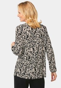 Langemouwblouse in een zwart en beige abstract patroon, gemaakt van lichte stof met een vloeiende snit en zijsplitten voor meer bewegingsvrijheid.