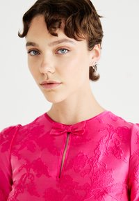 Pink dress with textured floral pattern, keyhole neck with a bow detail, short puffed sleeves, and smooth sheen finish.
