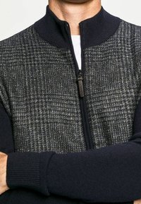 Gestrickter Zip-Up-Pullover mit einem strukturierten grauen und marineblauen Muster, geripptem Kragen und Bündchen. Verfügt über einen zentralen Reißverschluss und Handtaschen.