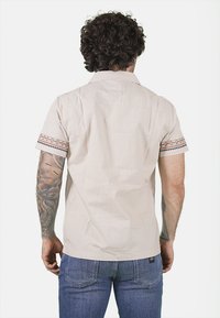 Camicia beige chiaro a maniche corte con colletto alla francese, caratterizzata da ricami decorativi sulle maniche. Realizzata in tessuto morbido e testurizzato.