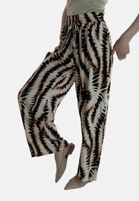 Wijd uitgesneden broek gemaakt van lichtgewicht stof met een zwart en crèmekleurig zigzagpatroon. Elastische tailleband en zijzakken, gecombineerd met beige flats.