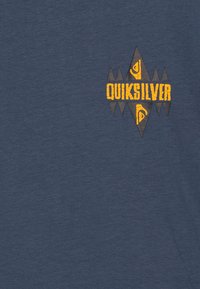 Camiseta azul marino con un logo geométrico en amarillo y negro de Quiksilver en el lado izquierdo. Material de algodón suave y texturizado.