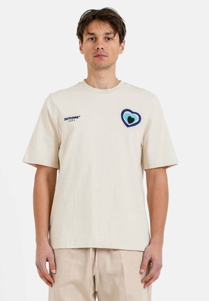 Beige bomulds t-shirt med korte ærmer, prydet med et flerfarvet hjerte broderet på brystet og en simpel rund halsudskæring.