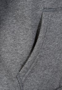 Tissu de sweat-shirt gris avec une poche avant, présentant une surface douce et texturée ainsi que des coutures visibles le long du bord de la poche.