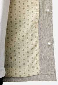 Tessuto esterno intrecciato grigio con bordo sfrangiato, che rivela una fodera interna color beige caratterizzata da un motivo geometrico ripetuto di punti e quadrati.