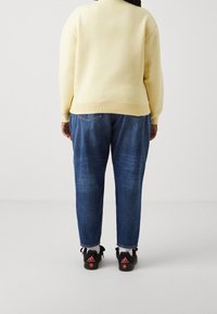 Sweatshirt jaune, jeans en denim bleu, baskets noires avec des accents roses. Présente un ourlet côtelé, des coutures d'épaule et un léger délavage sur les jeans.