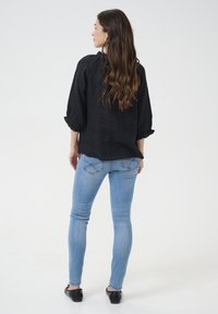 Blusa nera ampia con maniche a palloncino, abbinata a jeans skinny blu chiaro. Texture liscia e design semplice, senza motivi visibili.