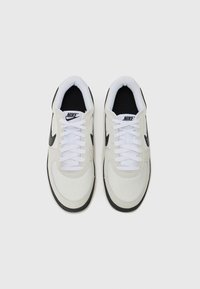 Nike tenisice s bijelim mrežastim gornjim dijelom, crnim akcentima, ravnim bijelim vezicama, podstavljenim okovratnikom i teksturiranom crnom gumiranom potplatom.