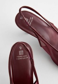 Burgundin väriset slingback-sandaalit, joissa on sileä nahkapinta, hienostunut nauhasuunnittelu ja brändimerkintä pohjallisissa.