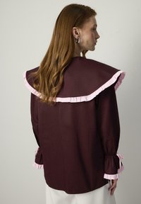 Bordeaux blouse met een grote gerimpelde kraag in lichtroze, met rimpelaccenten bij de manchetten en een ontspannen pasvorm. Soepele textuur, lange mouwen.
