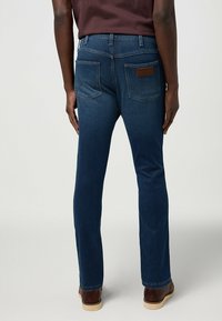 Donkerblauwe spijkerbroek met een rechte pasvorm, vijf zakken en een leren label op de achterkant van de tailleband. Gladde textuur, minimale details.
