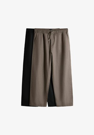 Dva páry bežných nohavíc s elastickým pásom a bočnými vreckami, jeden béžový a jeden čierny, zobrazené rozložené.