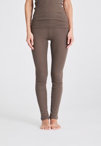 Braune, enganliegende Leggings aus strukturiertem Stoff, mit einem hohen Bund und einer glatten Verarbeitung, die sich zu den Knöcheln verjüngen.