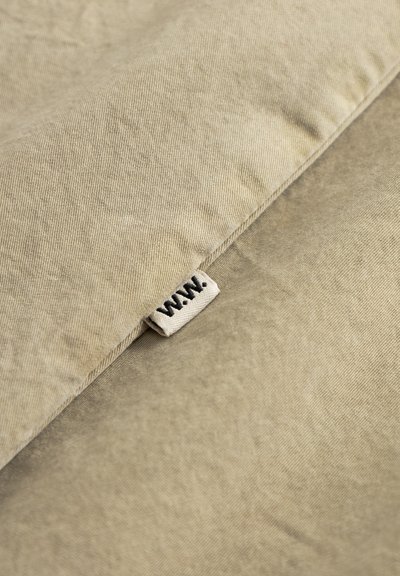 Beige fabric cushion with a textured surface, featuring a small sewn tag labeled “W.A.N.” near the edge.