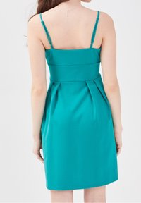 Robe sans manches turquoise avec un corsage ajusté, une jupe plissée et des bretelles fines. Tissu lisse avec un dos épuré et sur mesure.