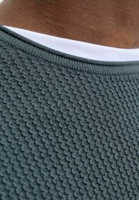 Pull gris texturé à manches courtes avec un col côtelé, doté d'un col intérieur blanc en contraste. Le tissu présente une surface tissée et à motifs.