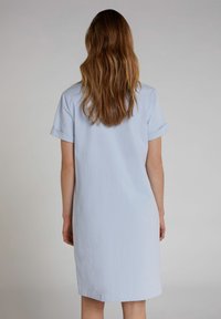 Lichtblauwe jurk met korte mouwen en een relaxte pasvorm, met opgerolde mouwen; gemaakt van zachte stof, heeft een rechte zoom en een minimalistisch ontwerp.