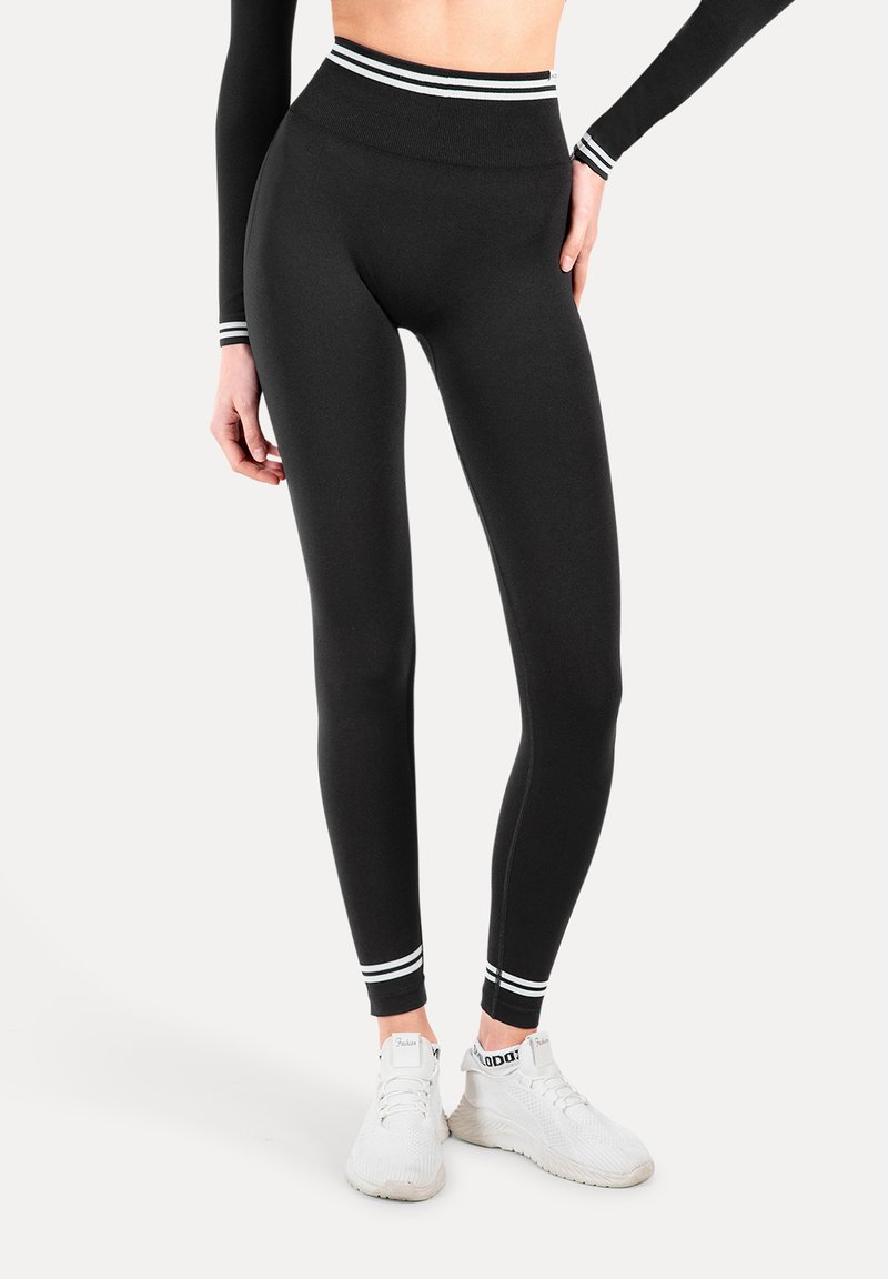 Zwarte leggings met hoge taille en witte streepaccenten bij de tailleband en enkel. Gemaakt van rekbaar materiaal voor actieve activiteiten.