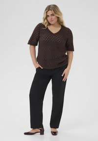 Brown knit short-sleeve sweater with a V-neck, paired with black high-waisted trousers and burgundy low-heeled shoes.