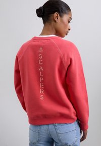 Sweat-shirt en coton rouge avec un col rond et des poignets côtelés, arborant un texte embossé "SCALPERS" dans une couleur contrastante au dos.