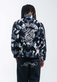 Fleecejacka i svart, blå och vit kamouflage med en stor drake och ros broderi på baksidan, med krage.