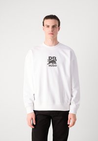 Hvit bomullssweatshirt med en svart grafisk logo "PR HUGO" og en silhuett av en okse på forsiden. Rund hals og ribbestrikkede mansjetter.