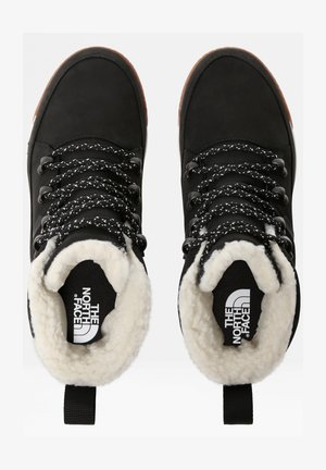 Botas de tornozelo à prova d'água pretas, com forro de pele sintética, tecido texturizado, atacadores com padrão preto e branco, e uma alça na parte de trás.