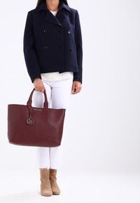 Granatowa marynarka podwójnie zapięta, biały top, białe dżinsy, bordowa torba na ramię z logo i zawieszką, miętowo-zielone botki do kostki o miękkiej teksturze.