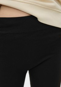 Leggings noirs à côtes avec une large ceinture, conçus avec une texture douce pour le confort. Superposés sous un haut de couleur claire.