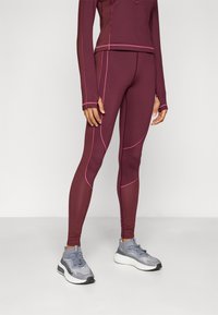 Mørkebrun idrettsantrekk med langermet topp og tights. Har rosa sømmer, teksturert stoff, og er kombinert med grå løpesko.