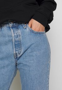 Jeans in denim azzurro chiaro con vita alta, dotati di tasche anteriori, cuciture visibili e una leggera texture effetto vissuto.