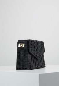 Borsa a tracolla nera intrecciata con una forma strutturata, dotata di chiusura a pattella e dettagli in oro. Esterno testurizzato con un design sofisticato.