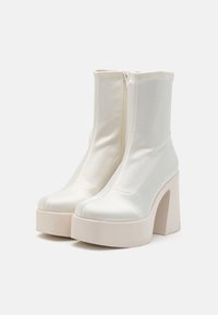 White ankle boots made of satin with a smooth texture, featuring a high block heel and a side zipper for closure. Platform sole design.