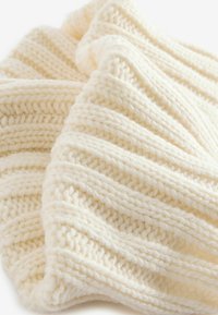 Cremfarbener gestrickter Stoff mit einem strukturierten, gerippten Muster. Weiche Wollzusammensetzung mit dicken, erhabenen Maschen.